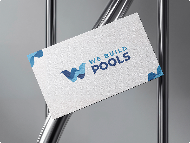 Business card with 'We Build Pools' logo on a metallic surface.