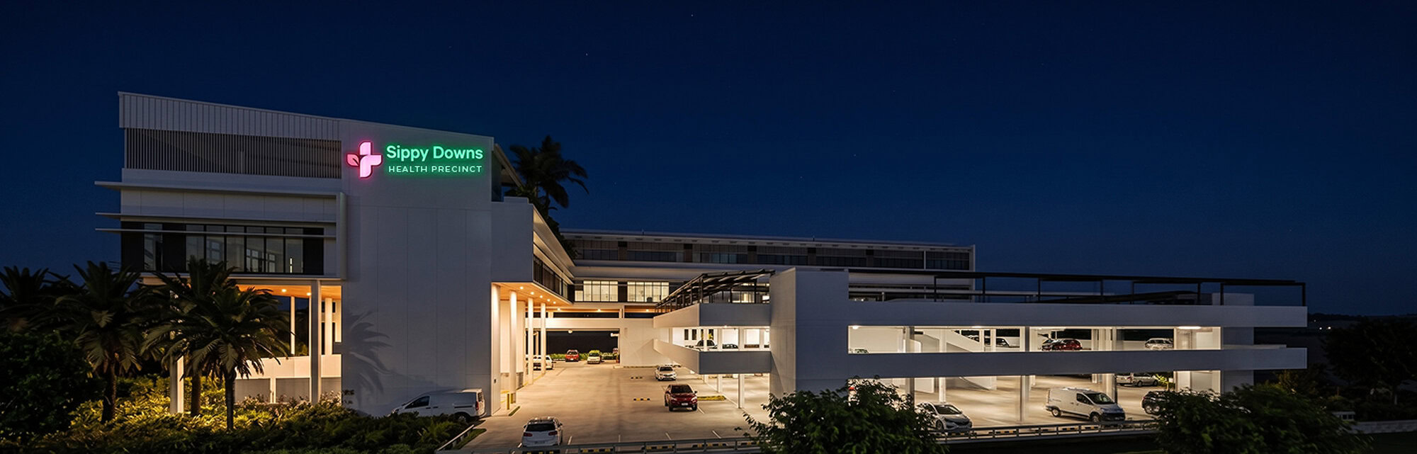 Sippy Downs Health Precinct building illuminated at night with signage visible.
